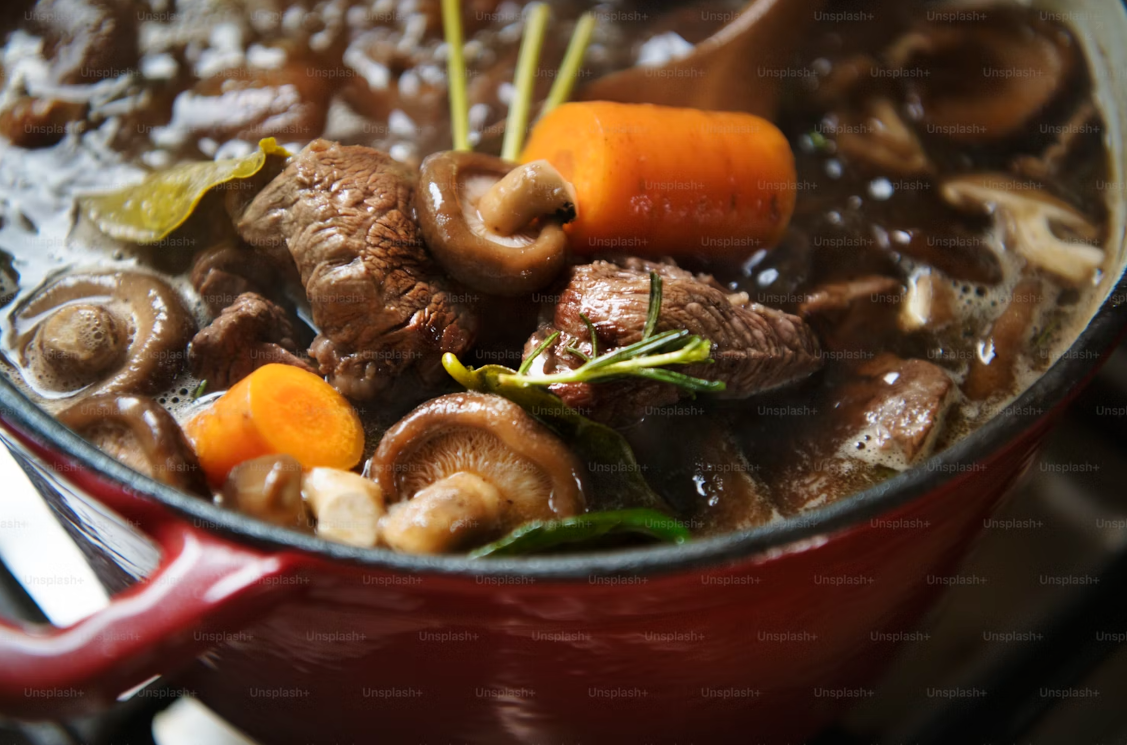 A hearty Beef and Barley Stew in a red pot, with tender beef, mushrooms, carrots, and fresh herbs simmering in a savory broth. Ideal for slow cooking.