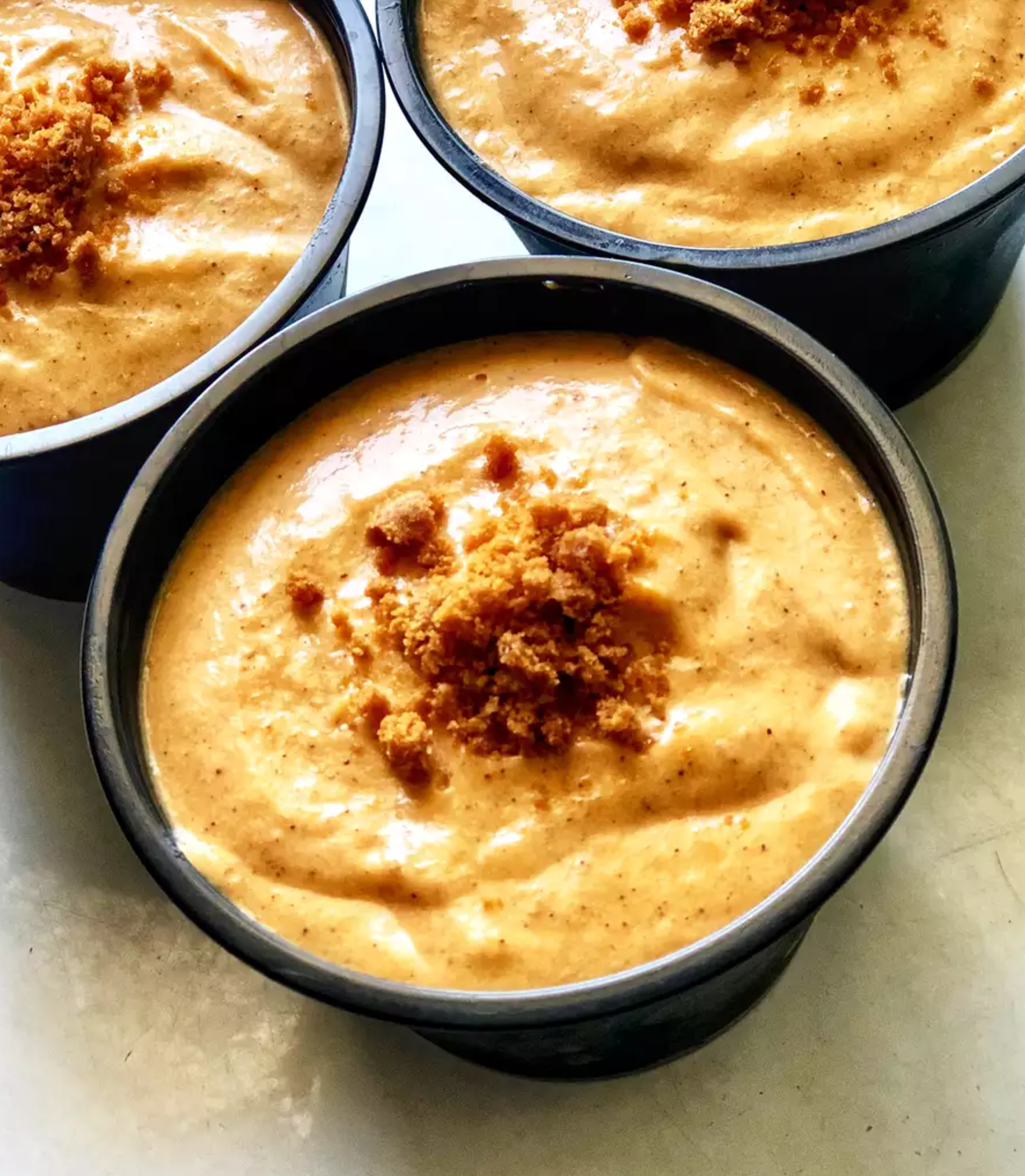 Three bowls of creamy savory pumpkin dip topped with crumbled spices, showcasing a rich and smooth texture perfect for appetizers or snacks.