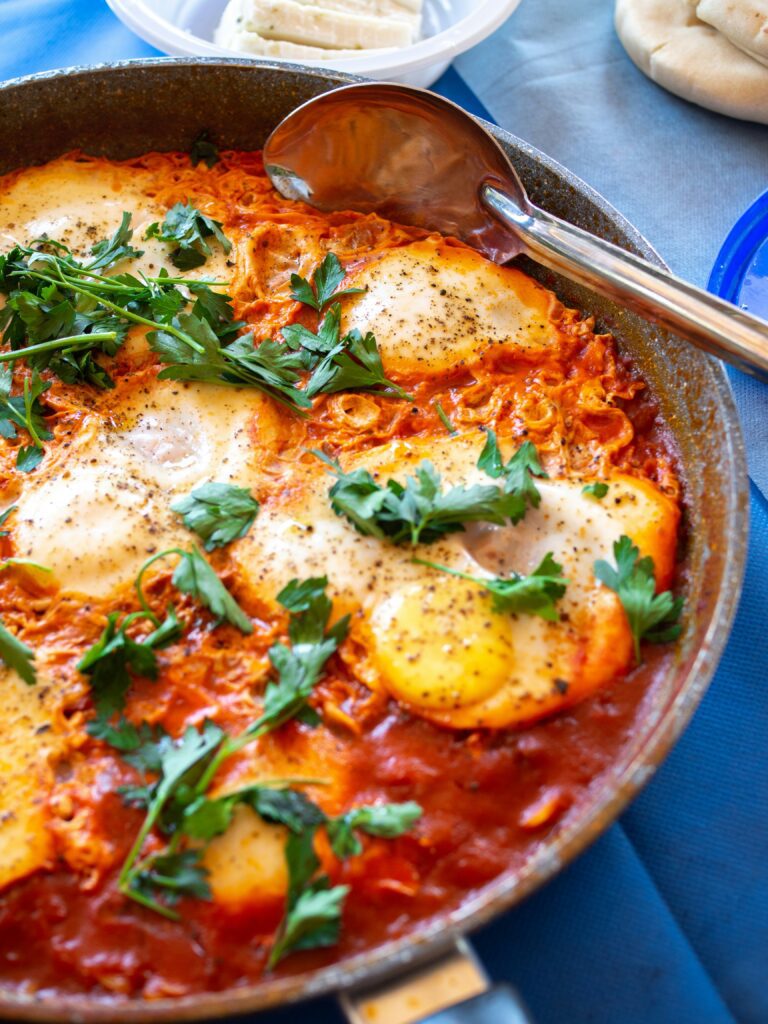 Algerian Chakchouka (Shakshuka) served in a skillet, featuring poached eggs nestled in a spiced tomato and bell pepper sauce, garnished with fresh parsley.