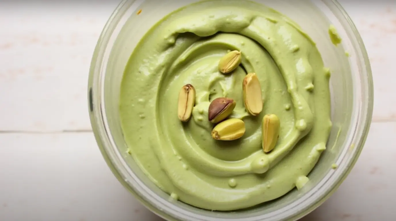 A jar of homemade pistachio cream with fresh pistachios and a spoon for spreading.How to Make Pistachio Cream 3